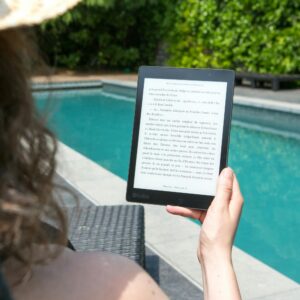 A woman relaxes by the pool, reading an e-reader for leisure. Perfect summer relaxation.